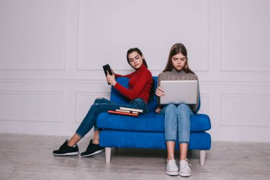 Boğazlı kazaklı kadın, iş yerinde rahat bir koltukta otururken dizüstü bilgisayarına bakıyor.