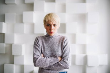 Elleri bağlı genç bir kadın kameraya bakıyor beyaz duvarın yanında boş vakit geçiriyor ve ışık odasında küp süslemeler yapıyor.