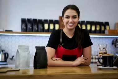 Gülümseyen esmer kadın kasiyerin yarım boy portresi. Perakende satış yapmaktan ve çalışma yerinde servis yapmaktan zevk alıyor.