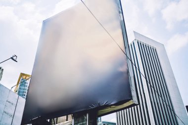 Gündüz vakti modern şehrin caddesinde bulunan çağdaş yüksek binalar arasındaki siyah, parlak, boş reklam panosunun altından.