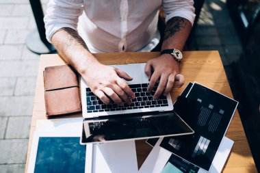 Uzaktan çalışma sırasında kağıt ve tabletle masada otururken netbook 'ta yazan isimsiz bir erkek çalışanın üstünden.