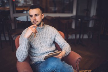 Düşünceli, sakallı, rahat giyimli bir adam. Dalgın dalgın bakıyor ve modern kafedeki iş projesini düşünüyor.