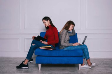 Uzun saçlı, rahat kazaklı ve kot pantolonlu, mavi otobüste sırt sırta oturan ve konsantre olan uzun boylu kadınların yan görüntüsü.