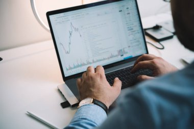 Yukardan gelen tanınmayan erkek finansör dizüstü bilgisayarla klavyede yazı yazarken modern ofiste rapor hazırlıyor.