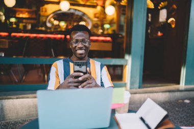  Optik gözlüklü dişlek adam cep telefonunu mesaj yazmak ve göndermek için kullanıyor.