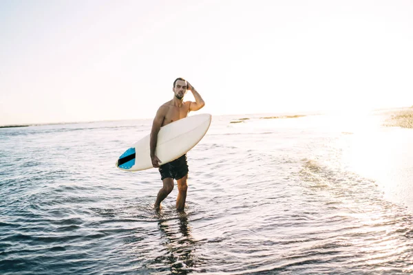 Okyanustaki spor antrenmanından sonra sahilde sörf yapan beyaz profesyonel sörfçü. Algarve 'de yaz tatilinin tadını çıkaran seksi genç adam.