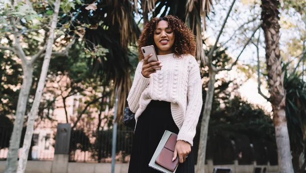 漂亮的深色皮肤女性穿着时髦的阅读短信和智能手机在城里的广告 — 图库照片