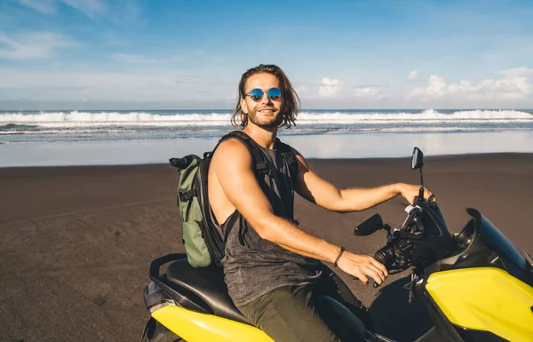 熱帯のビーチの間にバイクに座って 夏休みを楽しんでいる間にカメラを見ている下着の中で陽気な髭を生やした男性オートバイ家 — ストック写真