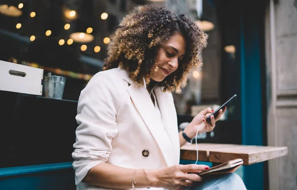 Elektronik kulaklıklı güzel kadın nesli Z planlama için ders kitabı ve ağ kurmak için modern cep telefonu aygıtı tutuyor.