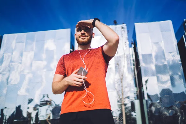 Cheerful Male Athlete Sportswear Earphones Mobile Phone Listening Music While — Stock Photo, Image