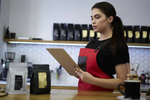 深刻なCaucasianブルネット女性Baristaでエプロン保持請求書チェック会計にBarでコーヒーショップ — ストック写真