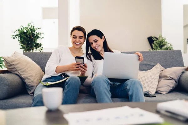 Kanepede rahat rahat gülümseyen, akıllı telefonları paylaşan ve kanepede birlikte gülen kızlar.