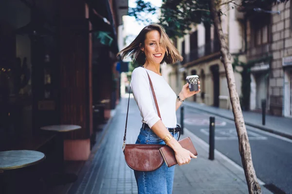 Gülümseyen beyaz bir kadının yarım boy portresi gündelik giysiler giyer aromalı kahvenin ve tatillerde şehir merkezinde boş zamanların tadını çıkarır.