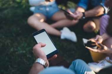 Yüzsüz erkek, bir elinde boş ekranla akıllı telefon tutarken bir yandan da parkta arkadaşlarıyla dinleniyor ve dinleniyor.