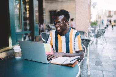 Optik gözlüklerdeki mutlu erkek kullanıcı dizüstü bilgisayar teknolojisiyle blog yayını oluşturmak için uygulama yüklüyor