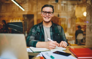 Her ne kadar kafeteryadaki not defterine notlar yazarak kameraya bakan serbest giyinmiş genç ve neşeli bir erkek olsa da.