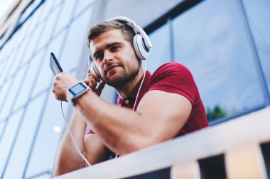Genç ve yakışıklı bir adam, balkonda dinleniyor. Kulaklıkla müzik dinliyor. Bulanık arka planda akıllı telefon kullanıyor.