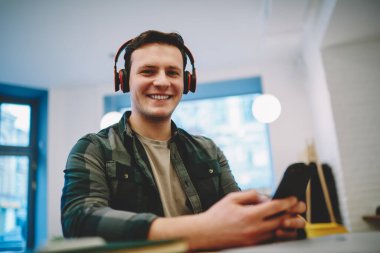 Düşük açılı, kablosuz kulaklıklı, müzik dinleyen ve molada cep telefonunda yazan pozitif erkek.