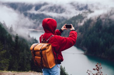 Kırmızı kıyafetli, kayalık kayalıklarda duran ve doğanın görkemli dağlık manzarasına hayran olan tanınmamış bir kâşifin arka planı.