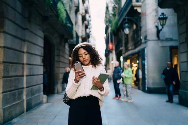 街の通りの読書メッセージやスマートフォン上のニュースに立って流行の摩耗で魅力的な暗い肌の女性 — ストック写真