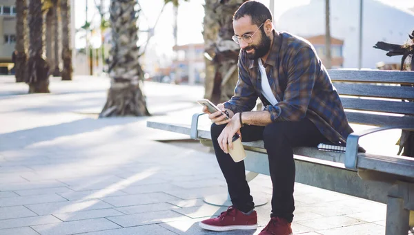 Güneş gözlüklü adam modern mobil cihazla solo seyahat hakkında bilgi arıyor.