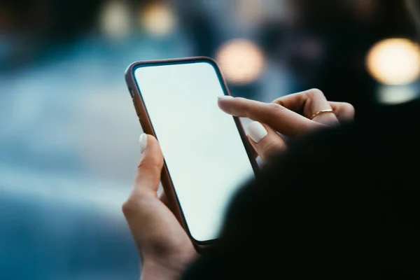 Crop unrecognizable young female choosing appropriate application on screen of digital mobile phone while enjoying free time on city street