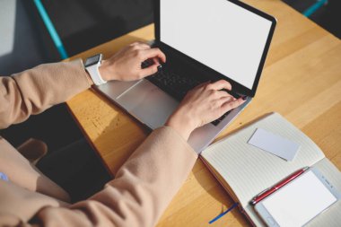 Yüksek açılı mahsul, elinde not defteri ve akıllı telefonuyla masasında otururken elinde boş ekran olan akıllı arama ağıyla tanınmayan bir kadın.