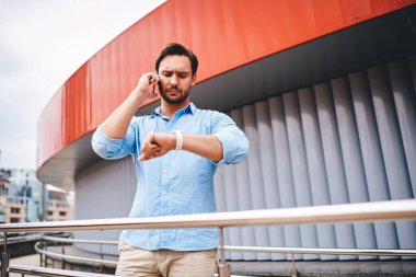 Düşünceli işadamı, dışarıda dikilirken meslektaşıyla izleme planlama toplantısını kontrol ediyor. Seyahat biletleri alan operatörle konuşurken nöbet tutan düşünceli bir erkek turist.