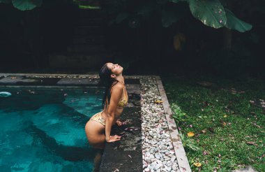 Yukarıdan bakıldığında, yaz tatilinde dinlenirken mayo giymiş, havuzda dinlenen çekici bir kadın görülüyor.