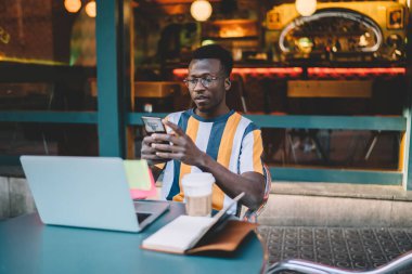 Milenyum Bilişim Uzmanı, gözlüklü kontrol uzmanı kaldırım caddesindeki kafede çalışan modern cep telefonu cihazıyla ilgili bilgilendirme aldı.