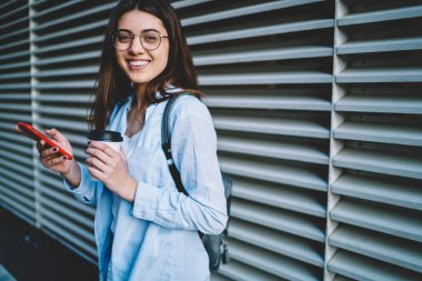 Şehir merkezlerinde cep telefonuyla gülümseyen neşeli bir kadının yarım boy portresi.