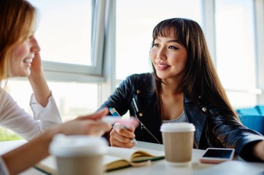 Neşeli Kafkas ve Asyalı öğrenciler eğitim kitabından bilgilendirme notlarını tartışırken gülümsüyorlar