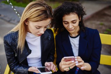 Gündüz vakti apartmanın yanında bankta otururken akıllı telefonlardan süzülen çok ırklı genç kadınların yüksek açısı