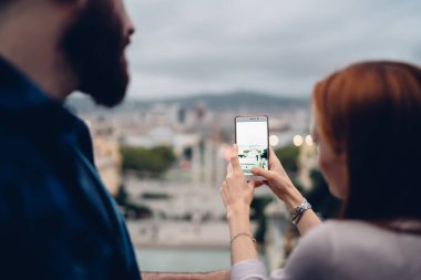 Tanımlanamayan erkek arkadaşıyla tatillerde şehir manzarasına tıklamak için cep telefonu kamerası kullanan kadın blogcunun arka görüntüsü