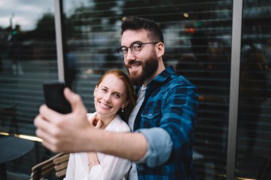  Mutlu hipsterlar cep telefonu medya uygulamasını kullanarak video bloğunu etkileyip sokakta poz veriyorlar.