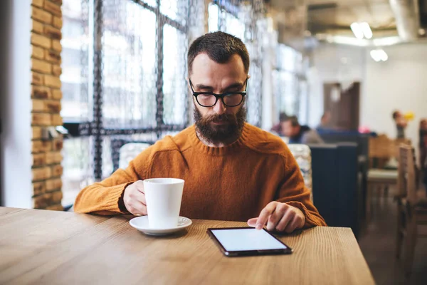 Focused Bearded Man Sweater Eyeglasses Touching Screen Tablet While Drinking — Foto Stock