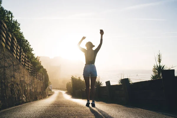 Gündelik giyimli, mutlu, beyaz tenli bir kadının arka görünüşü. El kaldırıyor, yaz tatillerinden zevk alıyor.