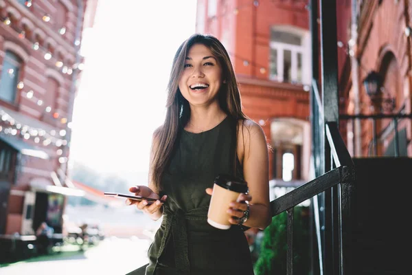 旅行中のカメラで笑顔移動するコーヒーとスマートフォンデバイスと陽気な女性ブロガーの半分の長さの肖像画 — ストック写真