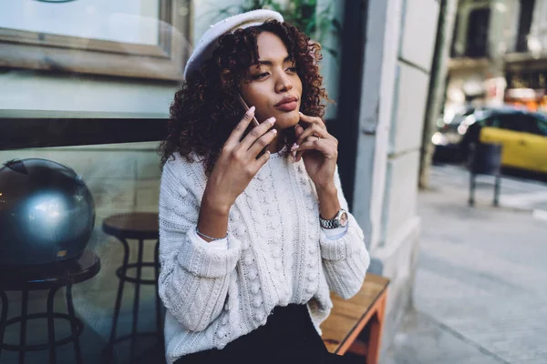 Sıradan giysiler ve kol saati takmış, sırıtan Afro-Amerikan kadın ahşap bankta oturuyor ve sokakta dinlenirken akıllı telefonuyla konuşuyor.