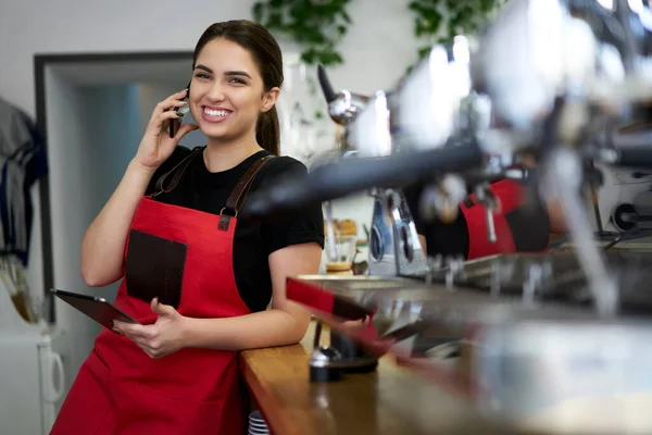 Усміхнена Брюнетка Офіціантка Уніформі Насолоджується Розмовою Мобільному Телефоні Роблячи Банкінг — стокове фото