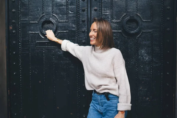 Şık giyinmiş şık bir kadın şehrin antik kapılarının yanında duruyor ve tek başına seyahat etmekten memnun bir şekilde gülüyor.