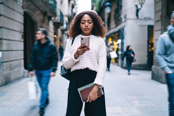 深刻な暗い肌の女性で流行の摩耗で歩く上の通りシェアコンテンツブラウジングウェブページ上のスマートフォン — ストック写真