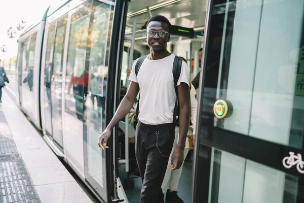 Happy dark skinned male dressed in trendy wear satisfied with public transport and traffic in town