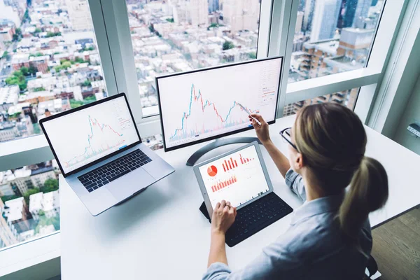 Resmi olarak anonim bir kadının yüksek açılı arka görüntüsü masada oturuyor ve kripto para birimi bitcoin grafiği ile çalışıyor.