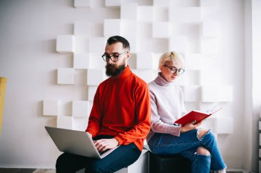 Dizüstü bilgisayarda çalışan sakallı bir erkek ve kadın serbest çalışan, gündelik kıyafetlerle notlarda notlar okuyan, açık modern işyerinde vakit geçiren biri.