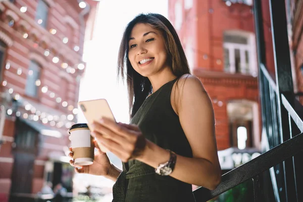 Happy Asian woman using smartphone application for wireless networking during coffee time in city