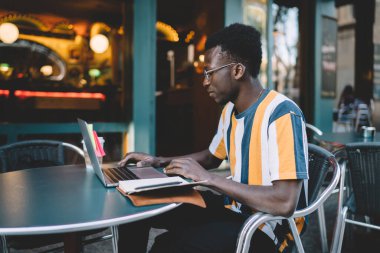 Koyu tenli yetenekli bir öğrenci ve eğitim programından öğreniyor. Sokaktaki kafede otururken internet bağlantısını kullanıyor.