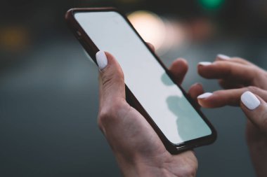 Tanımlanamayan, elleri manikürlü, modern cep telefonuyla sosyal medyada mesajlaşan, şehirde boş ekranlı, bulanık arka planlı bir kadın.