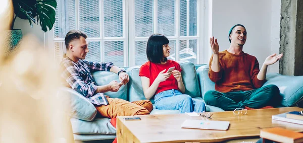 Düşünceli genç insanlar gündelik giysiler içinde yumuşak koltukta otururken ve modern çatı katında akıllı telefonlarla iletişim kurarken eğlenceli arkadaş hikayeleri dinliyorlar.