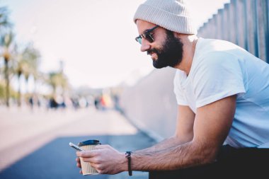 Kafein içeceği kullanan Ortadoğulu bir erkek bankacılık uygulaması ve hesap detaylarını kontrol etmek için akıllı telefon aygıtı kullanıyor